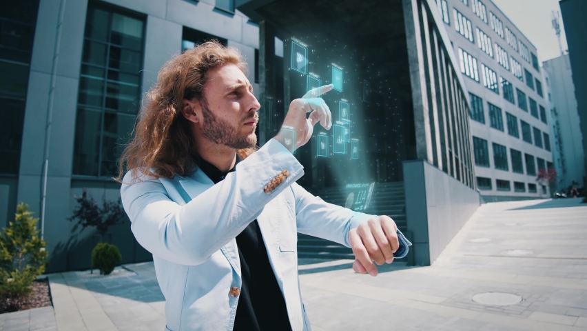 Curly-haired young businessman using smartwatch outdoors watching statistics analyzing data browsing holographic touchscreen. Techological innovation. Augmented reality. Future. - Powered by Shutterstock - Get 15% off with code: PIKWIZARD15