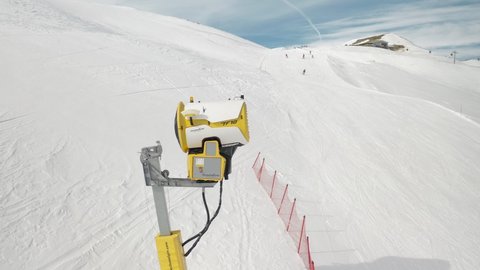 Livigno, Italy - February 21, 2022: Snow making machine, snow cannon at ski resort Livigno, Italy at snowy sunny winter day and skiers on background. 4k footage video