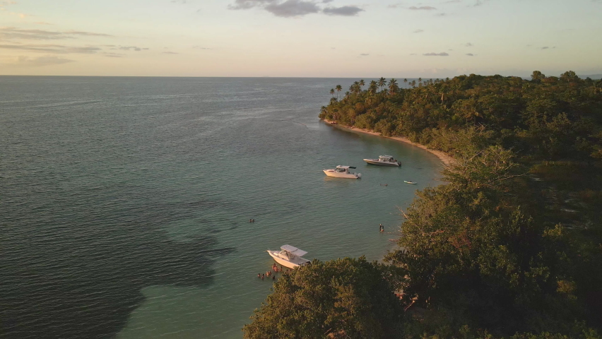 Flying drone over boats in crystal clear blue waters during sunset.