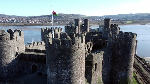 Medieval Conwy castle Welsh flag blowing on town ruins aerial view historical harbour orbit right