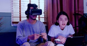 Asian couples wearing modern Virtual reality glasses sit use joystick play games in living room at home. Holiday Activity family entertainment technology. living together happiness. Concept meta verse