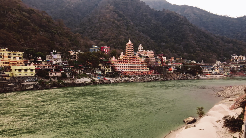 Aerial view of yoga capital city Rishikesh on a winter morning. Drone view of Laxman Jhula or Jhoola suspension bridge. Ganges or Ganga river view with temples on the shore in Rishikesh. Royalty-Free Stock Footage #1088132633