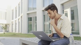 young man typing on his laptop sitting on a bench