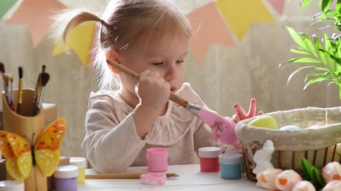 A two-year-old girl paints eggs for Easter with pink paint. Happy Easter.