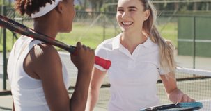 Video of happy diverse female tennis players holding rackets and talking. professional tennis training, sport and competition concept.