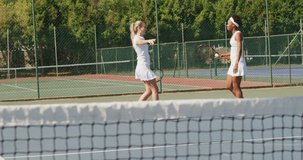 Video of happy diverse female tennis players holding rackets and embracing. professional tennis training, sport and competition concept.