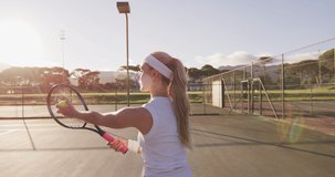 Video of back of caucasian female tennis player holding racket and hitting ball. professional tennis training, sport and competition concept.