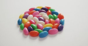 Video of close up of multi coloured sweets forming circle over white background. fusion food and sweets concept.