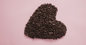 Video of heart formed with chocolate chip and copy space over pink background. fusion food, chocolate and sweets concept.