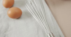 Video of overhead view of eggs and egg whisk on rustic cloth on beige background. fusion food, baking, eggs and easter concept.