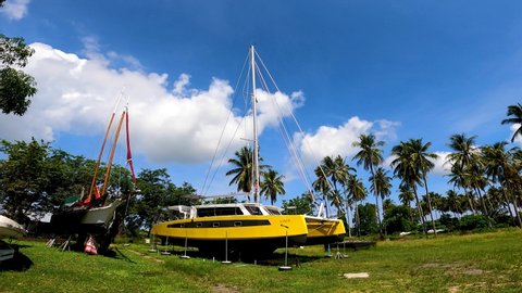 Phuket, Thailand, 02, March, 2022:
A yellow sailing catamaran stands on the stocks under repair in a dry dock, a yellow sailboat in a dry dock in the jungle under renovation