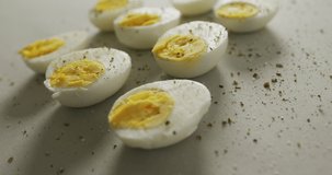 Video of close up of peppered halves of hard boiled eggs on grey background. fusion food, baking, eggs and easter concept.