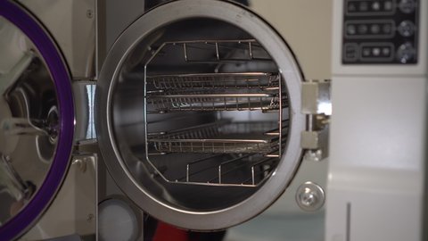 A woman puts a packaged instrument into an autoclave. Sterilization of instruments in a professional autoclave.