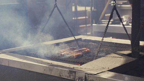 This video shows a bbq pit master brushing ribs with sauce as the grill smokes and cooks all of the fresh meat.