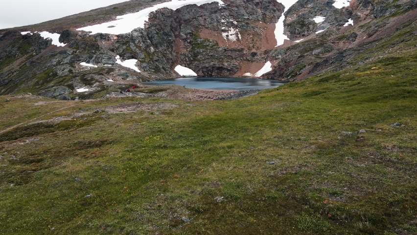Hikers sitting at the edge of the beautiful Crater Lake near the town of Smithers in British Columbia, Canada. Aerial flyover 