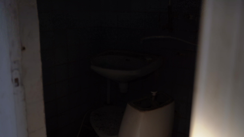 Sanitary unit of destroyed building, broken ceramic toilet bowl and sink. A man with a flashlight in a destroyed building. housing concept after the war