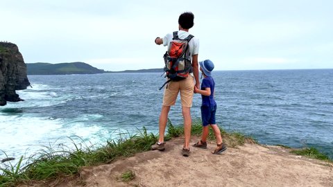 Vertical video. A young man and his son are on a hike among rocks near the sea. They are loooking at the sea. Slowmotion shot