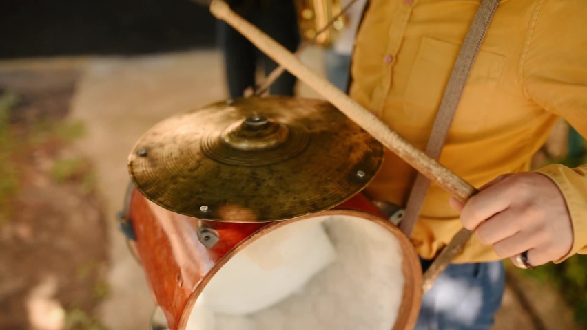 Close up drums on neck man. Hands holding drumsticks and beating outdoors. Portrait band members playing brass instruments on street during live concert. Ukrainian wedding traditions. Musician drummer