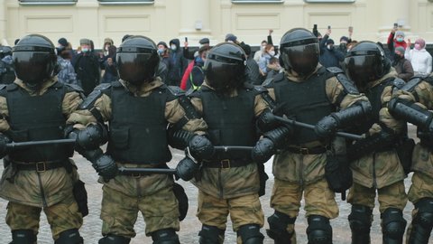 Geared and armored uniform, tinted visors on helmets, riot police team. Policeman officers with batons blocking streets for protesters by chaining arms. Enforcement group of police on demonstration.