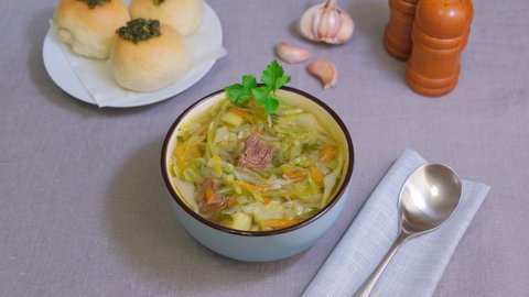 Shchi with pampushki (buns) and lard. Soup of cabbage, potatoes and meat. Traditional Russian and Ukrainian cuisine. Woman puts a board with lard on the table. Close-up, selective focus.