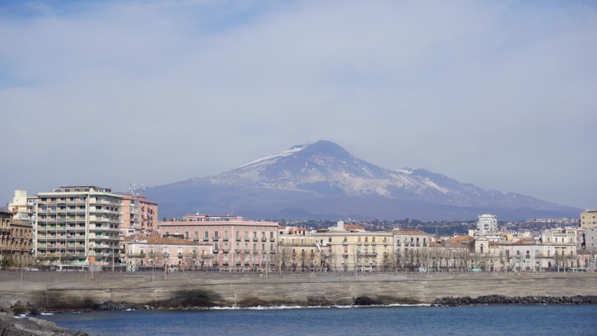 Time lapse of the clouds that flow over the sky of Catania, with the Etna volcano, the buildings, the train station and the sea