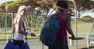 Video of back of diverse female tennis players holding racket, walking and talking. professional tennis training, sport and competition concept.
