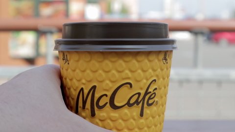 A man's hand opens a plastic lid drinker on a yellow paper coffee cup. Takeaway food. A man drinks hot coffee or tea at McDonald's fast food restaurant. Ukraine, Kiev - September 12, 2021.