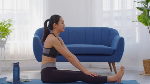 Athletic Healthy Asian woman in sportswear workout yoga sitting forward fold pose excercise on yoga mat at home in bedroom.Stretching muscle warm up before exercise.Healthy lifestyle concept