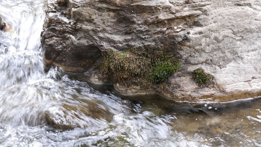 In the close-up we see the creek water rushing through the large mossy rock. A wonderful view of nature, a rushing stream. | Shutterstock HD Video #1088163143