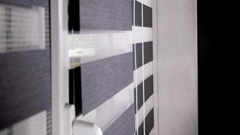 Woman hands closing rolling shutter or roller blind on a sunny day. Window roller duo system day and night. Close up on roll curtains indoor.