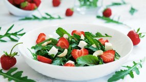 Vitamin salad of strawberry with arugula, spinach leaves, feta cheese and cashew nuts with salad leaves and fresh strawberry fruits around. Vegan food, keto diet and paleo diet. 4K, camera movement.
