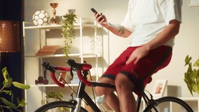 Sportsman riding bicycle and talking on video call, home gym. Young man cycling in living room with virtual conference, exercising. Spanish guy working out on stationary bike.