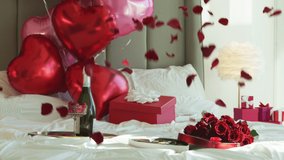 Super slow motion of falling red rose petals on white bed in elegant luxury hotel room with champaign red heart shaped balloons on background. Cinematic romantic background shot on RED camera 6K - Powered by Shutterstock - Get 15% off with code: PIKWIZARD15
