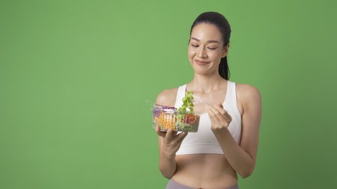 Portrait of Young Beautiful Sport Woman posing at Green Screen Background. She eating salad with smiling. Healthcare and Medical concept.