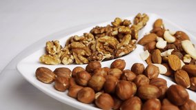 Various nuts close-up on a rotating white plate on a white wooden table. 4k raw video 60 fps.