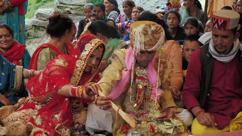 A Happy Indian bride and groom or a married couple dressed in ethnic attire are performing a ritual during a Hindu wedding ceremony in the countryside and rural area, Manali, India (March 2022)