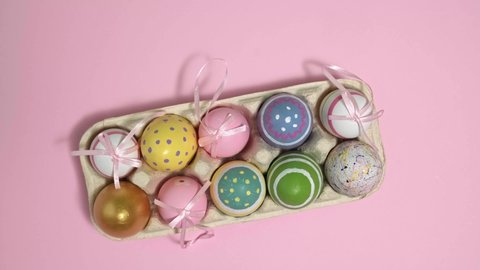 4k. Rotating colorful Easter eggs In A Cardboard Box on pink background. Eggs In A Paper Egg Container. Multicolored egg for Happy easter. Hello spring and Happy Easter holiday concept. Top View