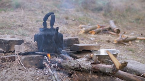 Old Black Smoked Kettle Warms Itself on the Grate of a Smoking, Fading Bonfire. Dirty coffee pot on a campfire. Boiling teapot on an open fire. Concept of adventure, travel, hiking, camping. Close up.