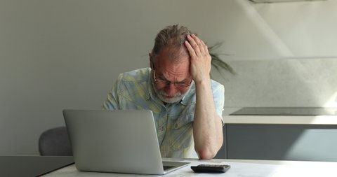 Senior man use laptop and calculator, calculates family budget feels angry, upset due to high taxes, huge household utilities need to pay. Bankrupt, insufficient old-age pension to pay bills concept