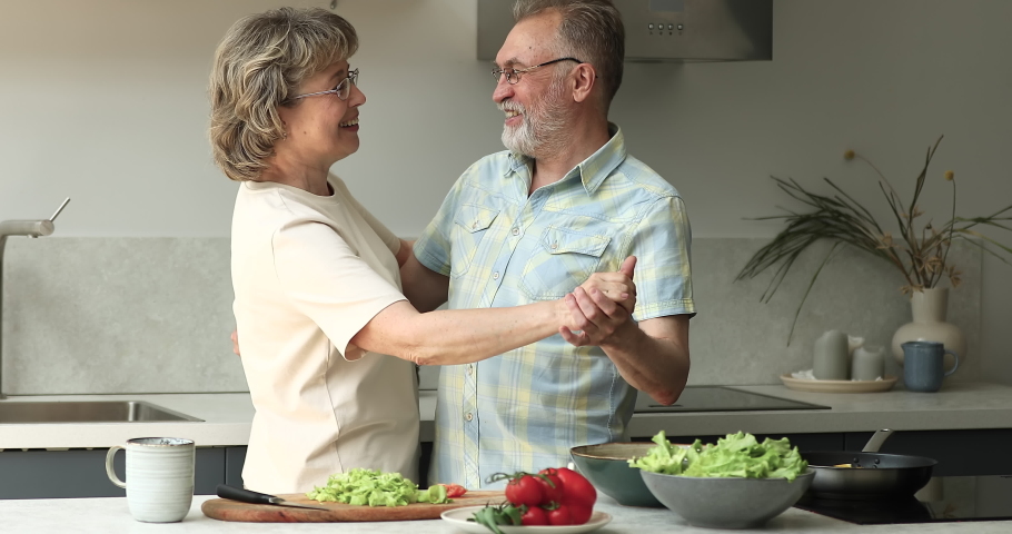 Attractive loving older couple dance in modern kitchen. Grey haired spouses listen music holds hands moving enjoy waltz on active weekend and carefree healthy retired life, relish hobby, love concept Royalty-Free Stock Footage #1088176019