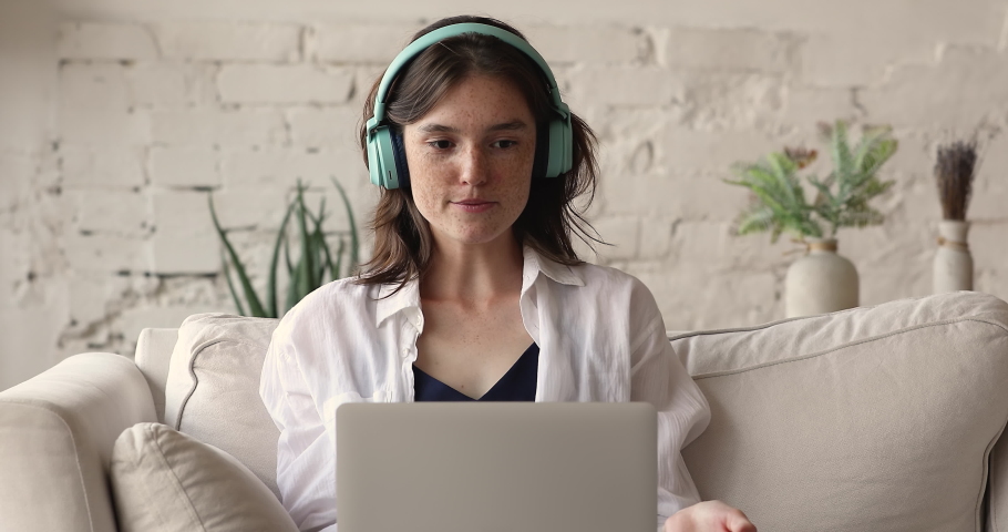 Confident young lady freelancer work from home wear earphones give advice consultation to customer before laptop screen speak to client remotely. Teen female chat in app for video call using pc webcam Royalty-Free Stock Footage #1088176075