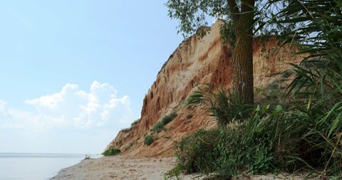 Empty desert sand, wild beach. Sea, ocean water panorama camera shot. Sandy cliff and rocky hill with orange ground soil and green tropical plants and wildlife. Exotic coastline and cloud background.