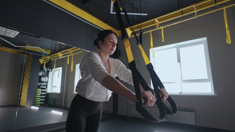 Sporty woman doing TRX exercises in the gym. Women training with fitness straps in the gym. Beautiful lady exercising her muscles sling or suspension straps.
