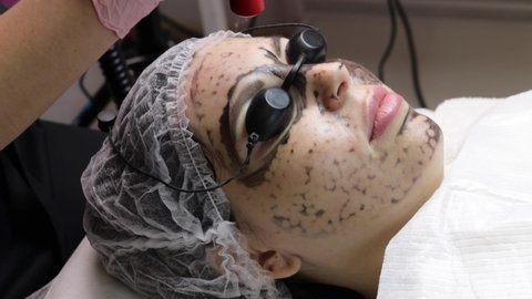 beautician applies black mask on face of beautiful woman. gorgeous woman in spa salon doing carbon peeling procedures for face.