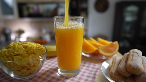Pouring fresh orange juice into a transparent glass on a rotating table in the kitchen, close up, slow motion. Cooking a healthy breakfast with natural organic vitamin drink