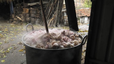 Traditional way of rendering lard and making greaves from a pork fat in large cauldron on a fire, outdoors in the village yard. Handheld shot footage