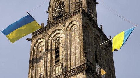 GRONINGEN, NETHERLANDS - 13. MARCH 2022: Ukraine flag waving on Martinitoren church above Grotemarkt close up.
