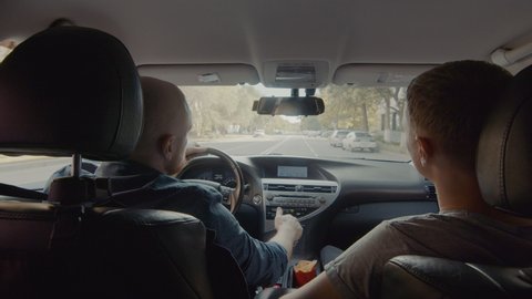 Rear view of two men sitting in the front seats of a car. The driver is distracted by the phone. Traffic rules