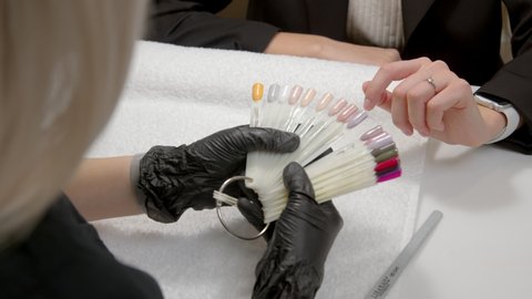 A close-up of a master doing a manicure to a young girl in a beauty salon. The client chooses the color of nail polish. The concept of nails, manicure, beauty, fashion.