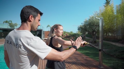 Young athletic fitness woman and personal trainer doing exercises to restore and strengthen the shoulder after an injury. In the park outside.